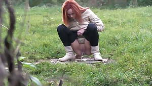 Kinky shameless redhead squats down to piss outdoors on the grass
